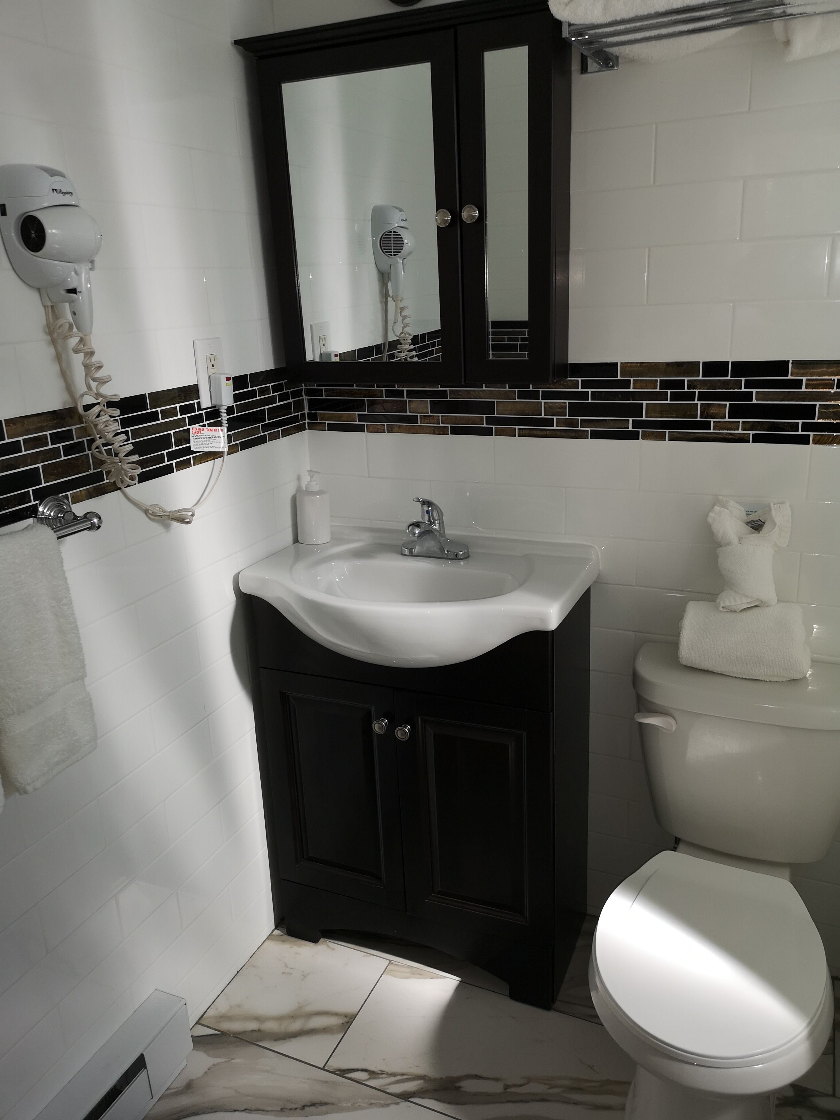 A bathroom with a white sink, dark cabinets, a mirror, and a toilet.