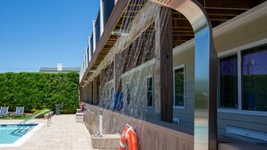 A modern building with a pool area, including a pool, lounge chairs, and a covered area with a water feature. - Aqualina Inn Montauk (Montauk)