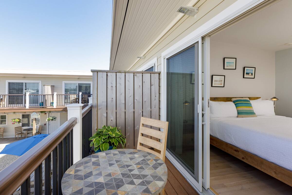 A balcony with a wooden railing, a round table with a geometric tile top, and a potted plant.