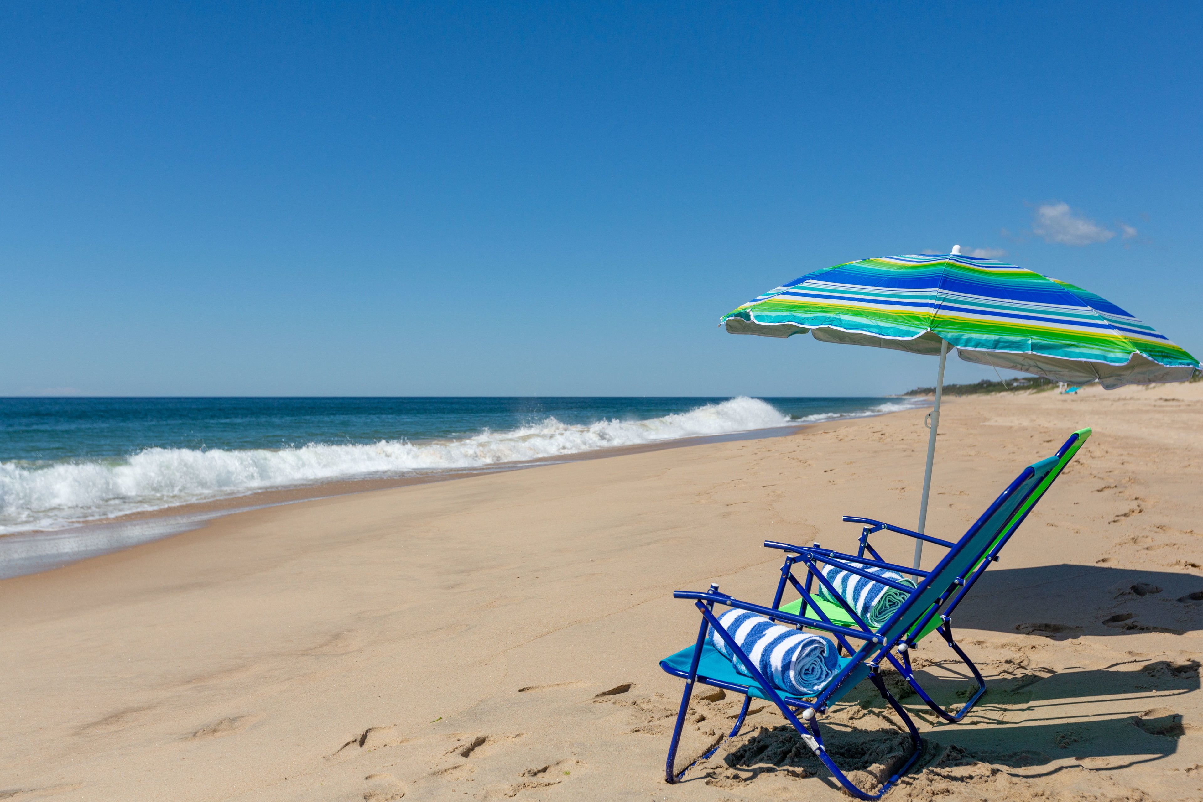 Una silla de playa con un paraguas a rayas sobre arena.