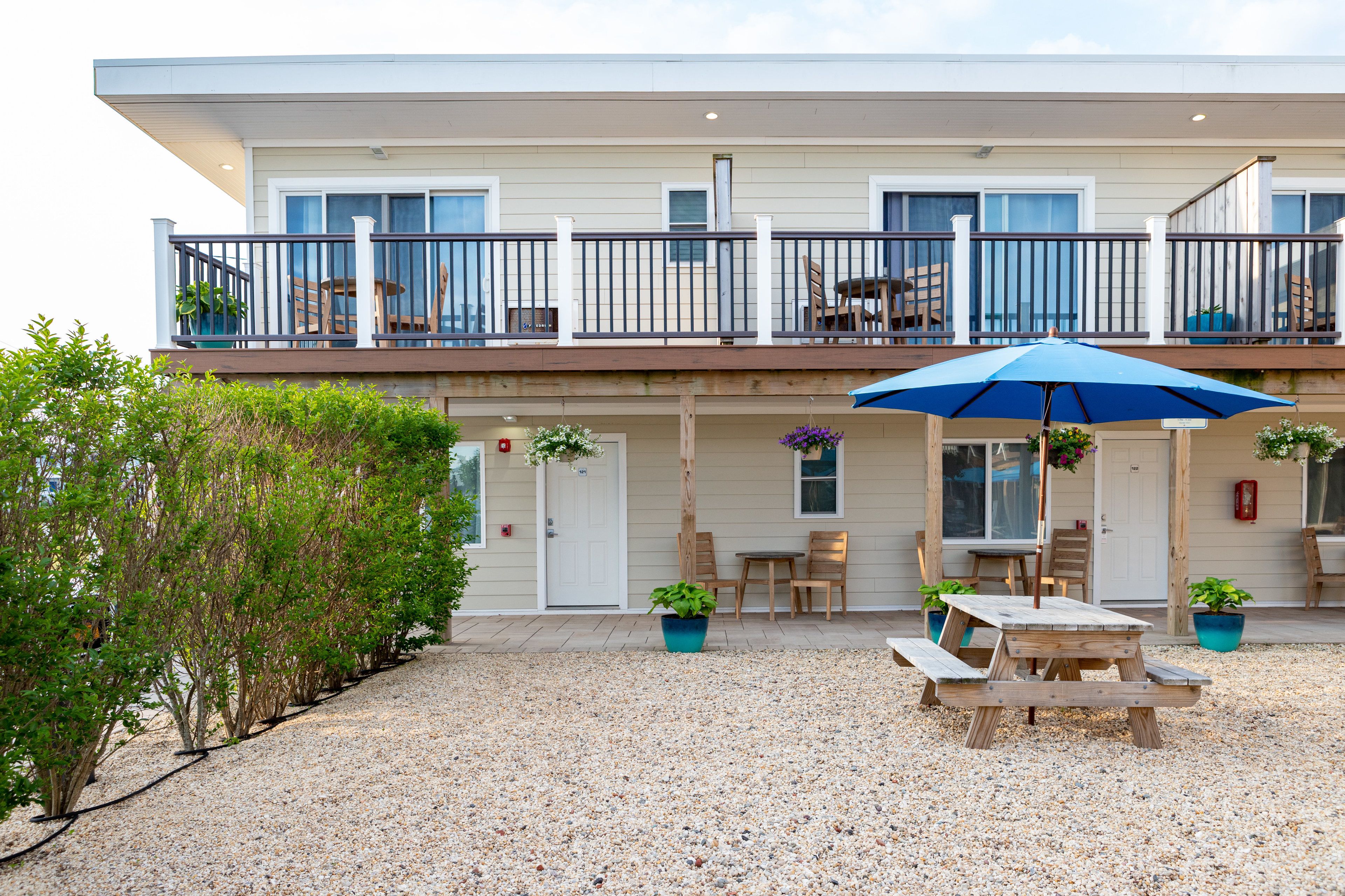 A two-story building with a balcony, outdoor seating, and a gravel patio.
