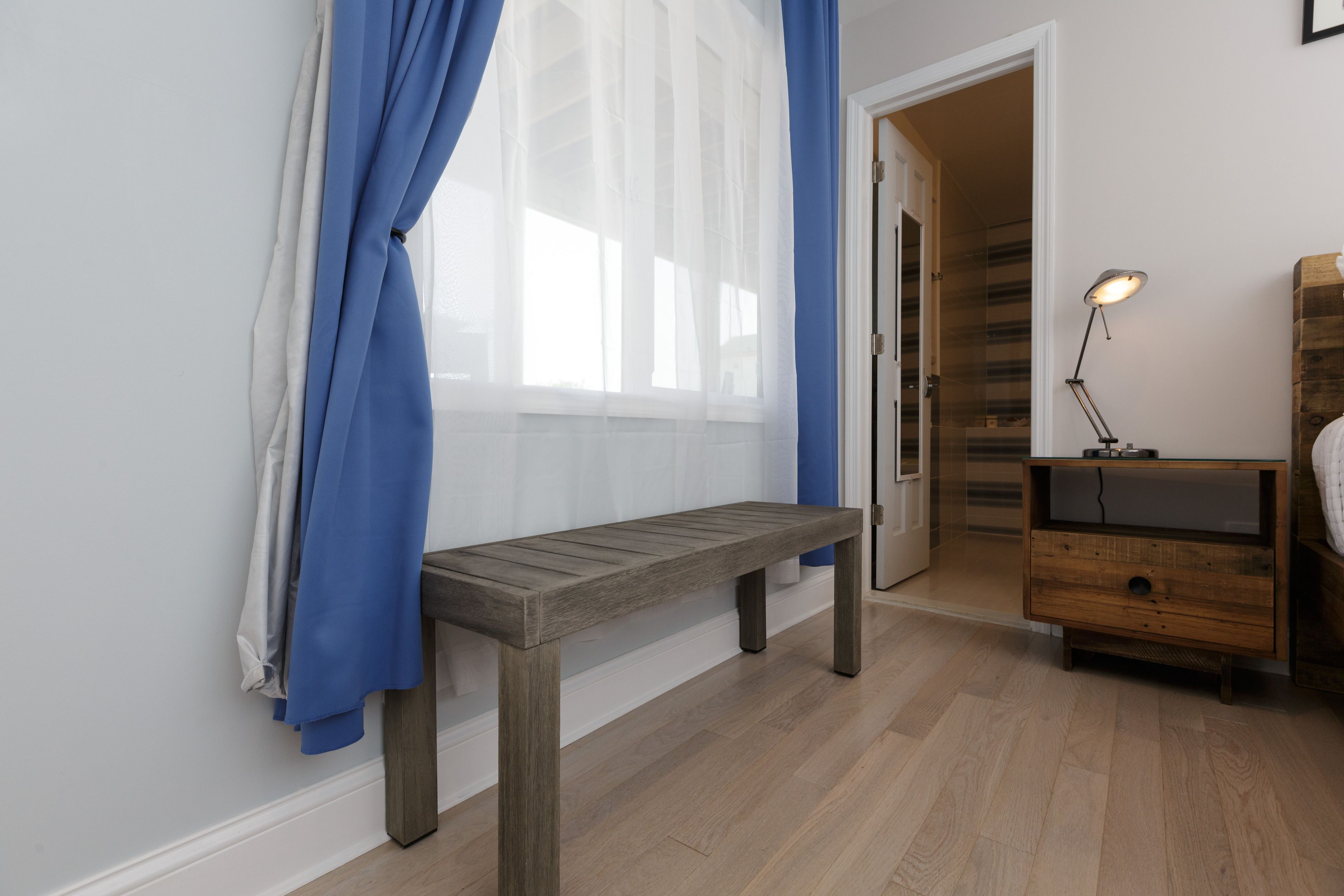 A bedroom with a wooden bench, a bedside table with a lamp, and a wardrobe.