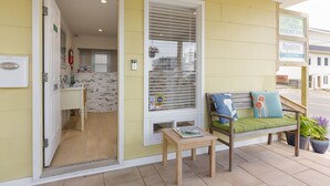 A check-in area with a wooden bench, a small table, and a window with blinds. - Aqualina Inn Montauk (Montauk)