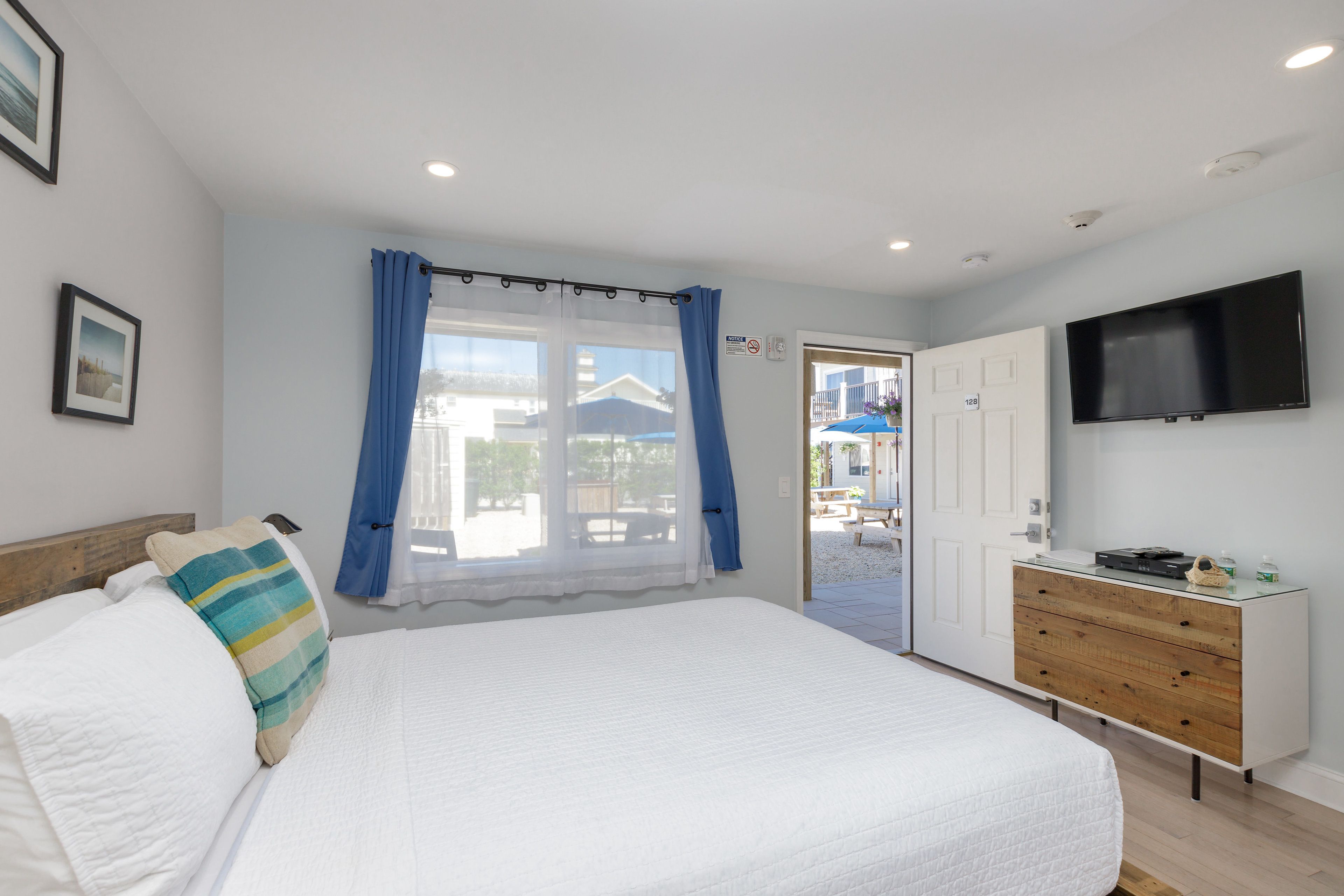 A bedroom with a large bed, a dresser, a flat-screen TV, and a window with curtains.
