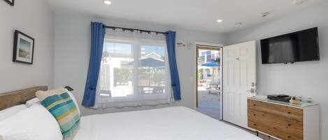 A bedroom with a large bed, a dresser, a flat-screen TV, and a window with curtains.