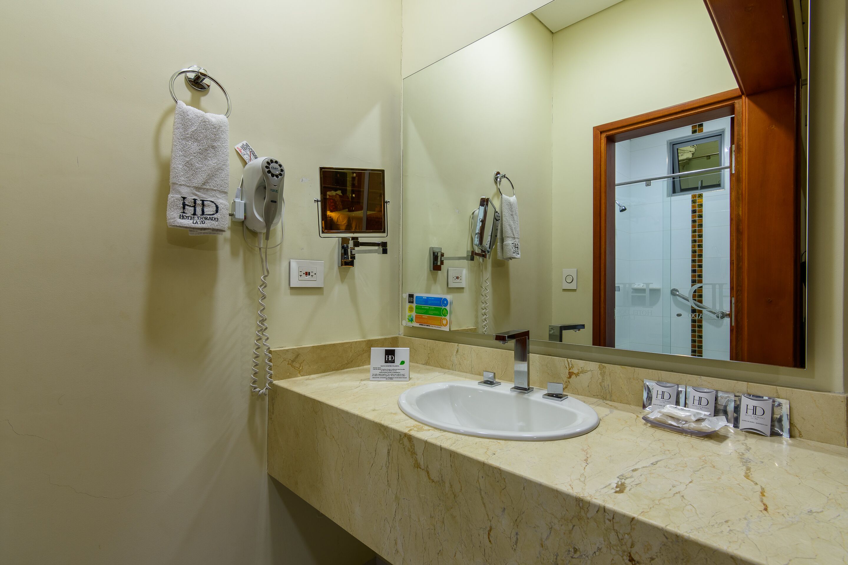 Une salle de bain d’hôtel équipée d’un lavabo, d’un miroir, d’un porte-serviettes et d’un sèche-cheveux.
