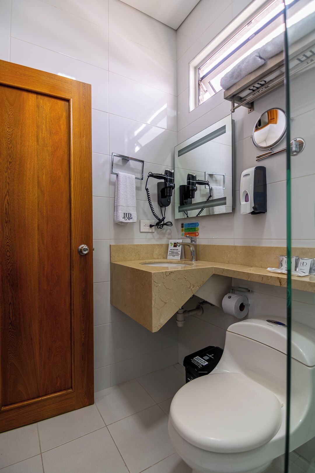 A bathroom with a wooden door, a white toilet, a sink with a mirror above it, and a towel rack.