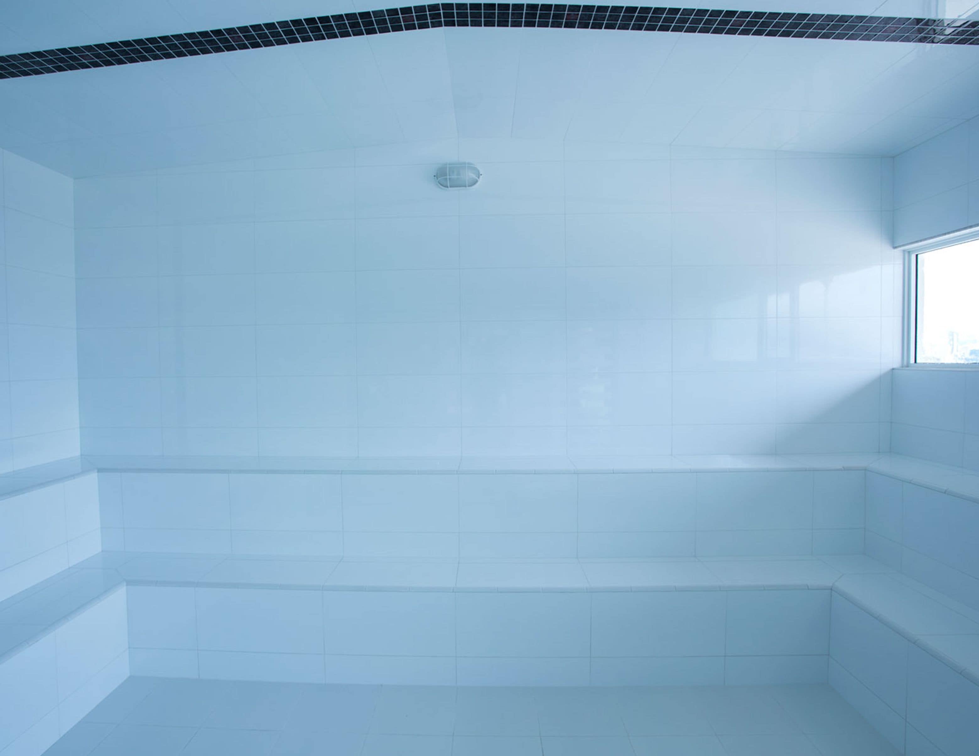 A bathroom with white tiles, a black-tiled ceiling, and a window.