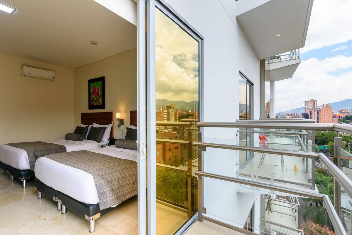 Een moderne hotelkamer met twee bedden, een balkon en stadszicht, en een groot raam.