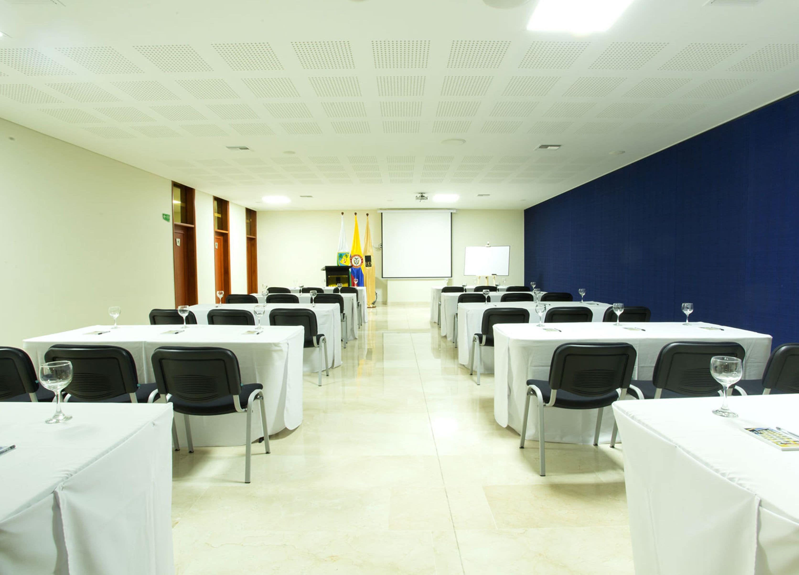 A conference room with rows of tables, chairs, and a projector screen.