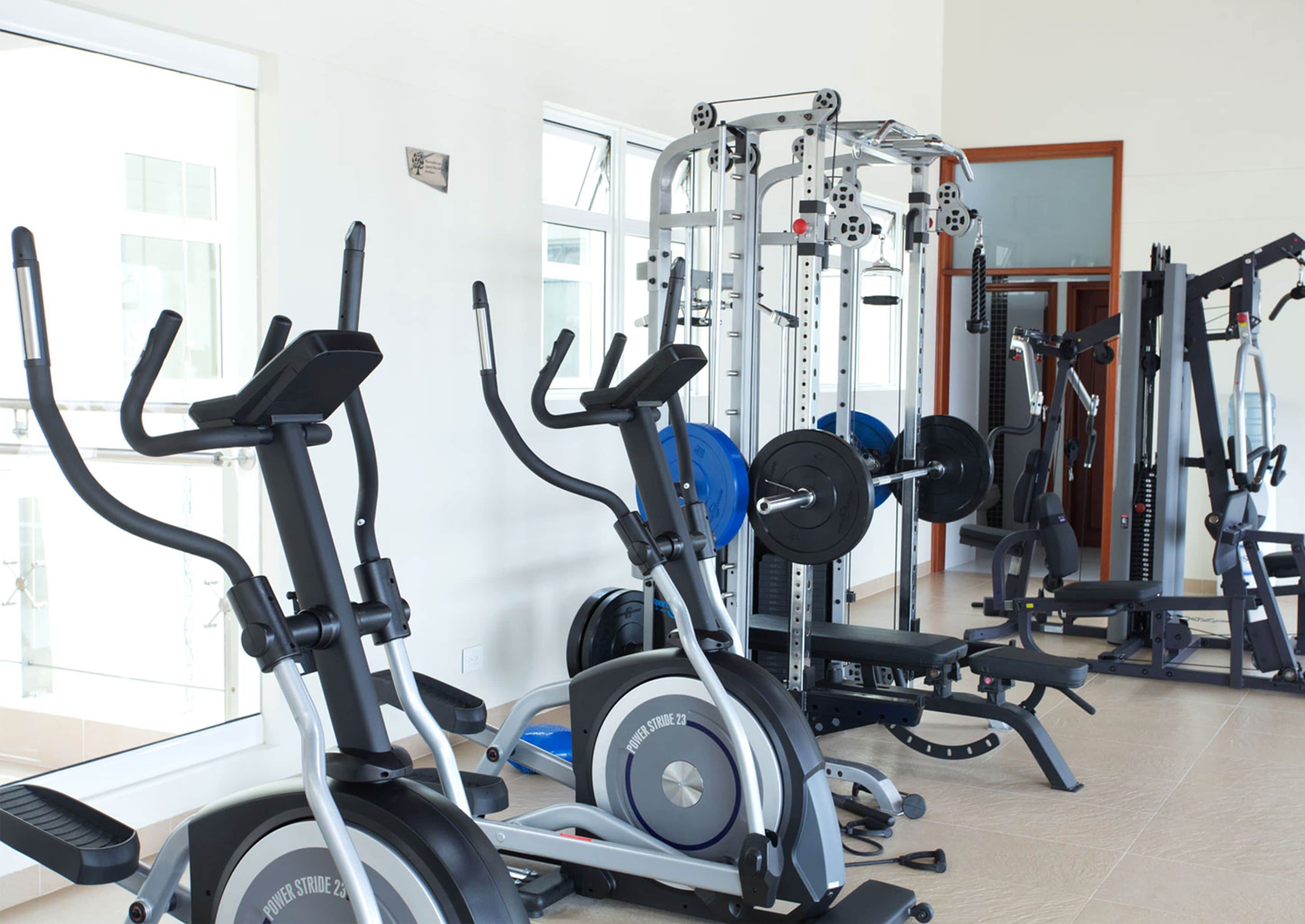 Une salle de sport équipée de matériel d’exercice, notamment des tapis de course, un banc de musculation et un support à squats.