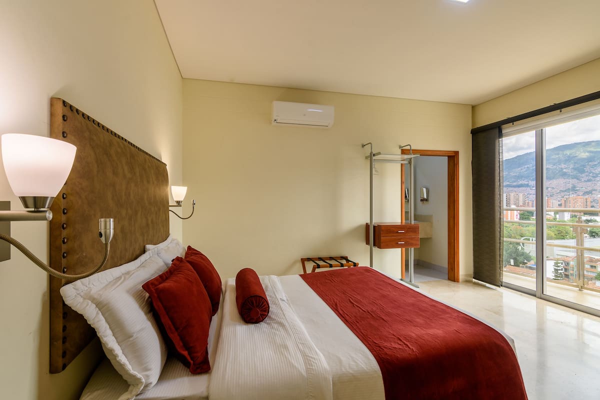 Hotelkamer met een groot bed, een bedlampje, een airconditioningapparaat, een badkamer met glazen deur en uitzicht op de stad.
