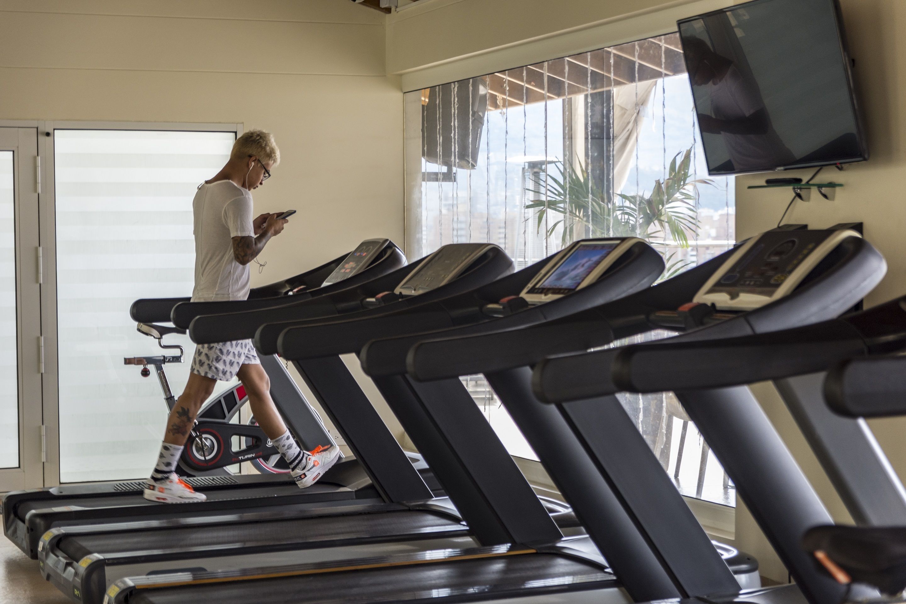 A gym with treadmills, a person using a treadmill, and a TV mounted on the wall.