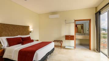Habitación de hotel con cama, mesita de noche, espejo, baño con lavamanos y vista a la ciudad.