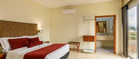 Habitación de hotel con cama, mesita de noche, espejo, baño con lavamanos y vista a la ciudad.