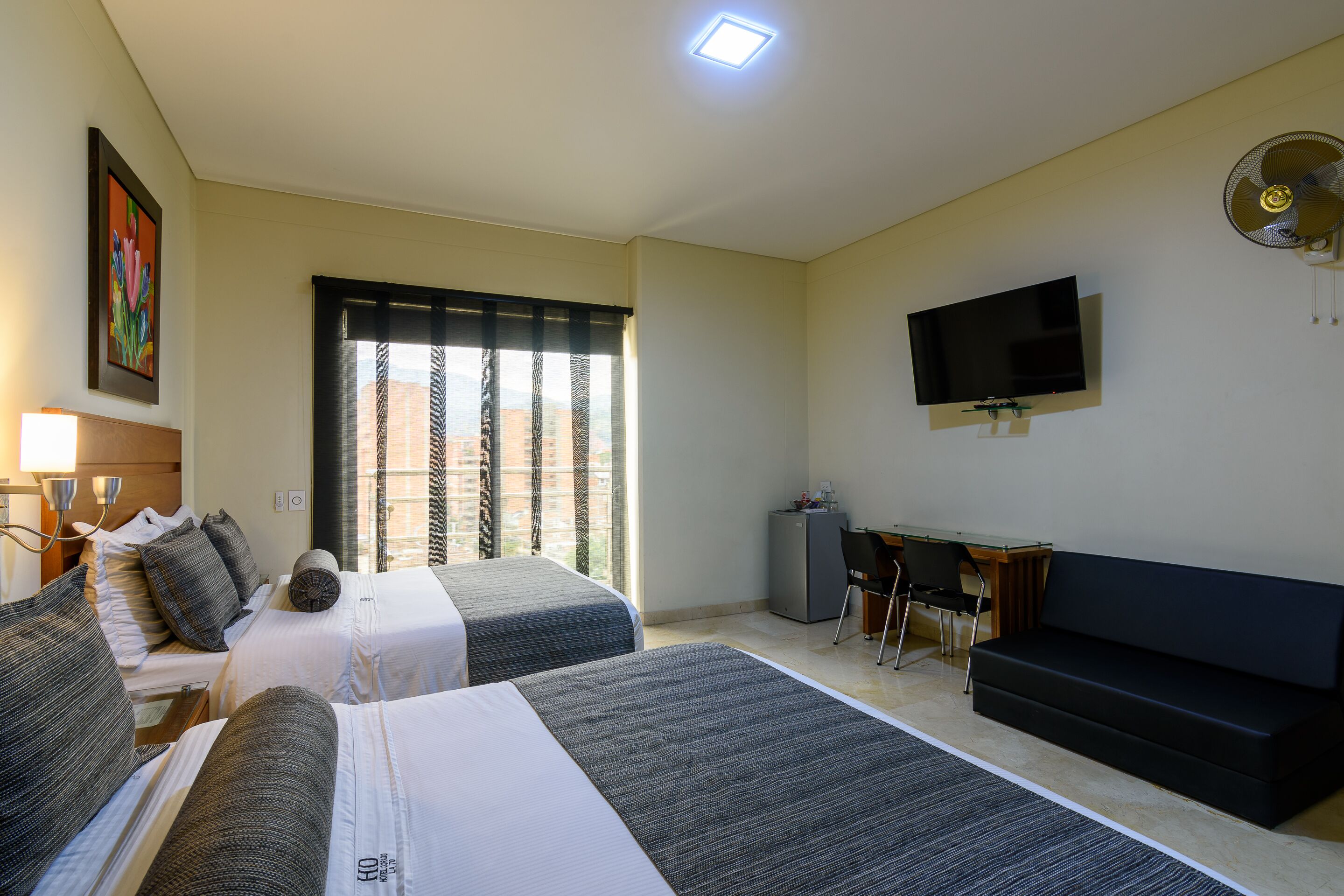 A hotel room with two beds, a desk, a TV, and a sofa.