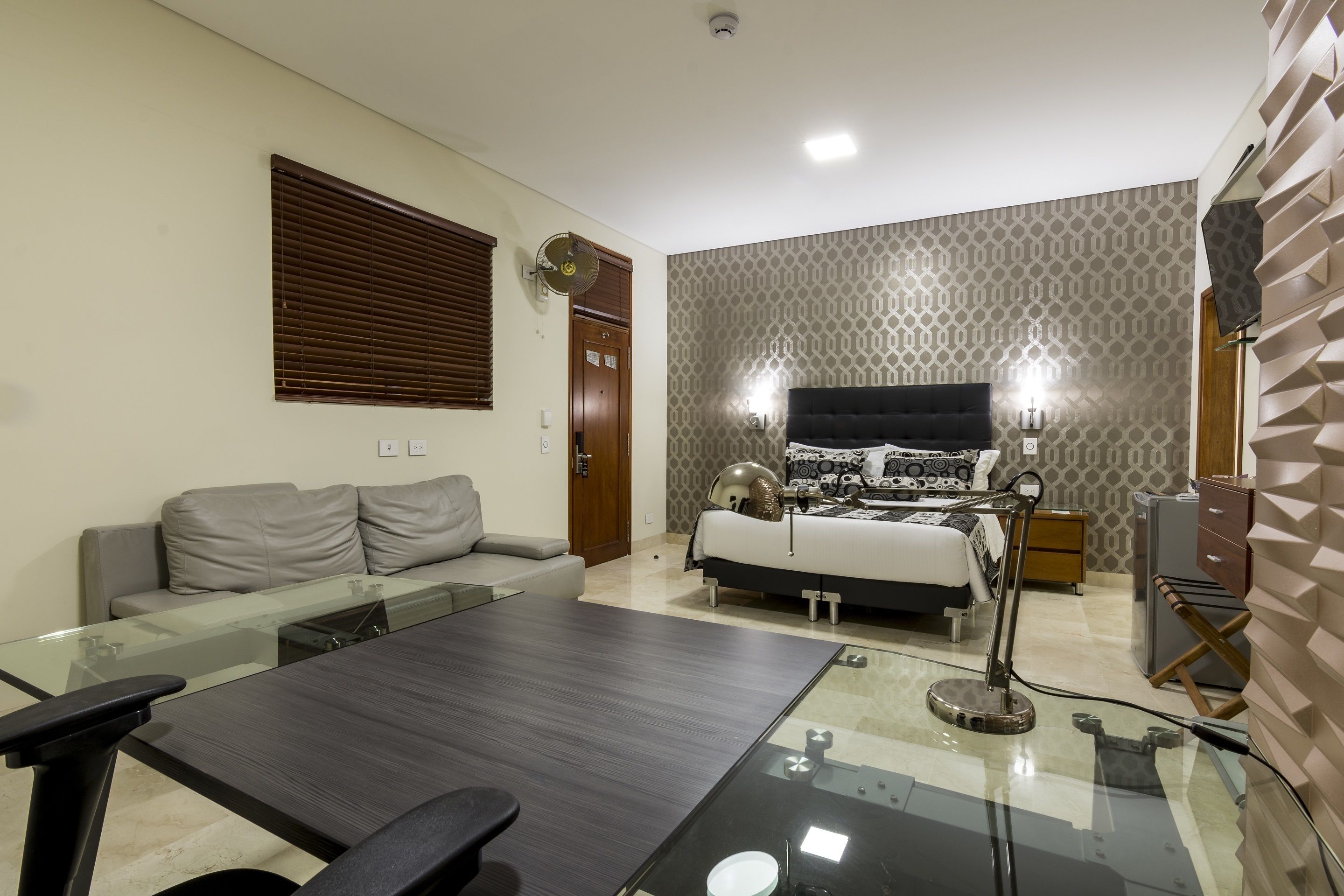 A modern bedroom with a bed, bedside lamps, a glass table, and a sofa.