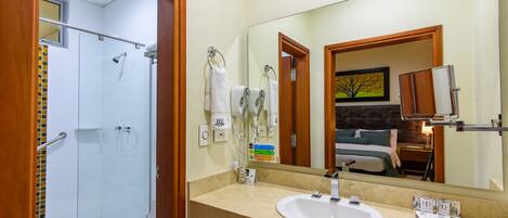 A hotel bathroom with a glass shower enclosure, a white sink, and a large mirror reflecting the room.