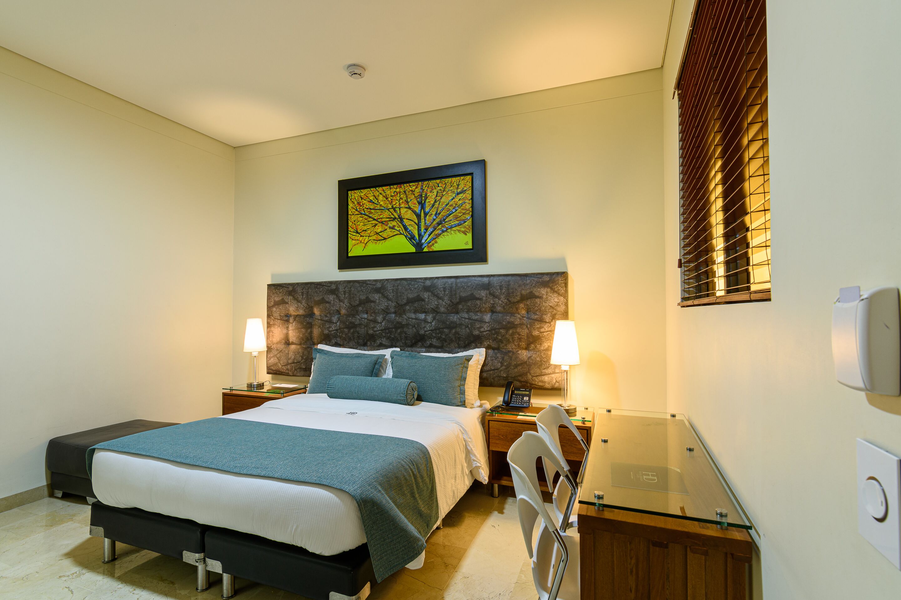 A modern hotel room with a large bed, two bedside tables, a desk, and a framed picture on the wall.