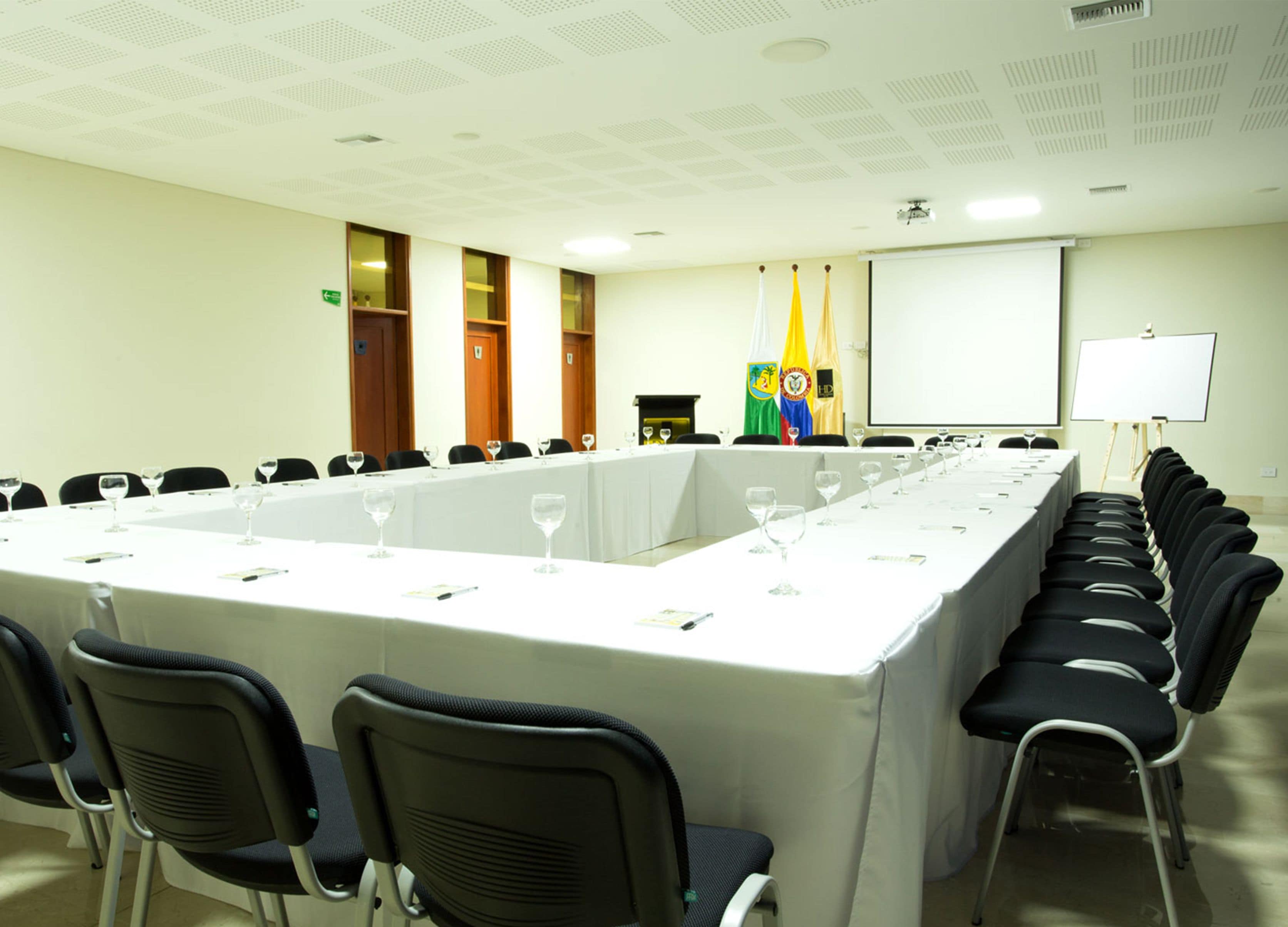 Un salón de conferencias con una larga mesa, sillas y una pantalla para proyector.