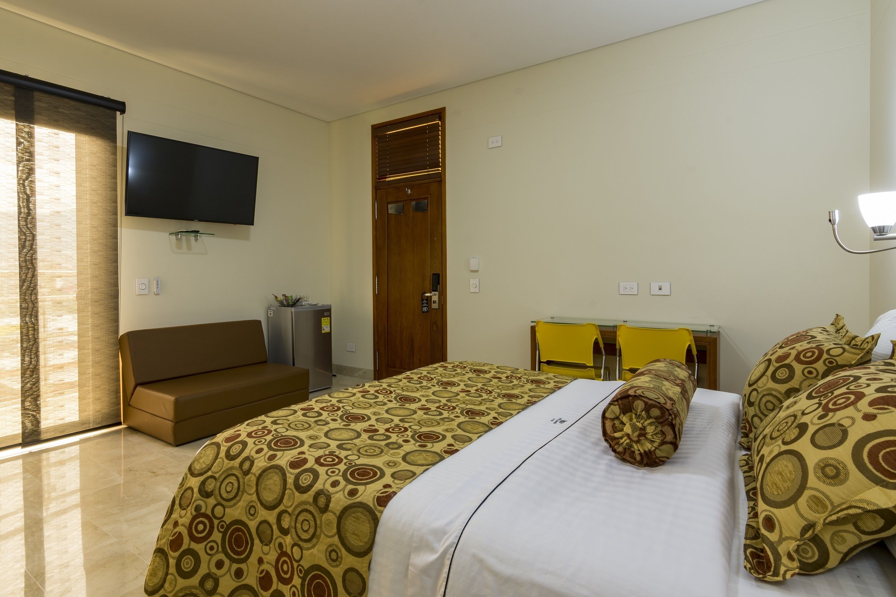 A hotel room with a bed, a sofa, a television, and a door.
