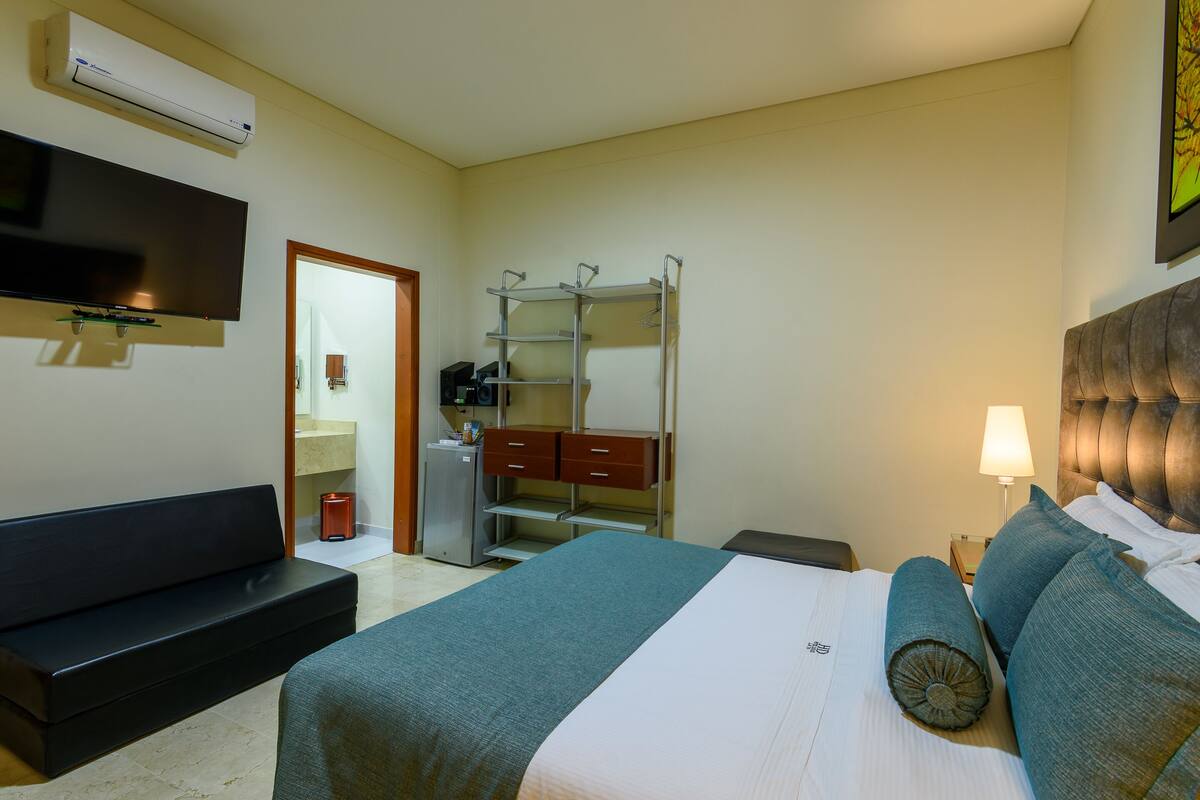Een hotelkamer met een bed, televisie, garderobe, bureau en lamp.