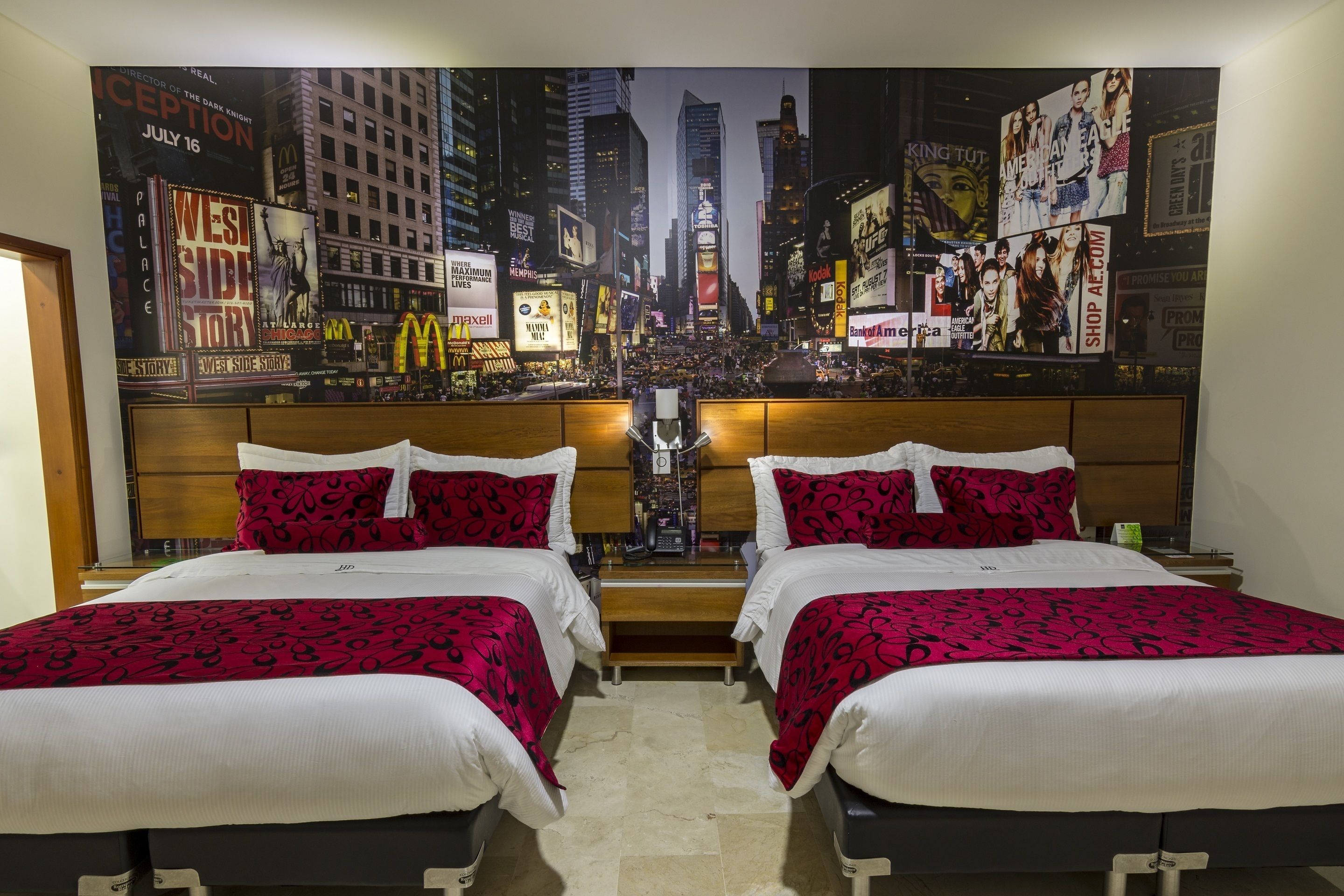 A hotel room with two beds, a cityscape mural on the wall, and a wooden headboard.