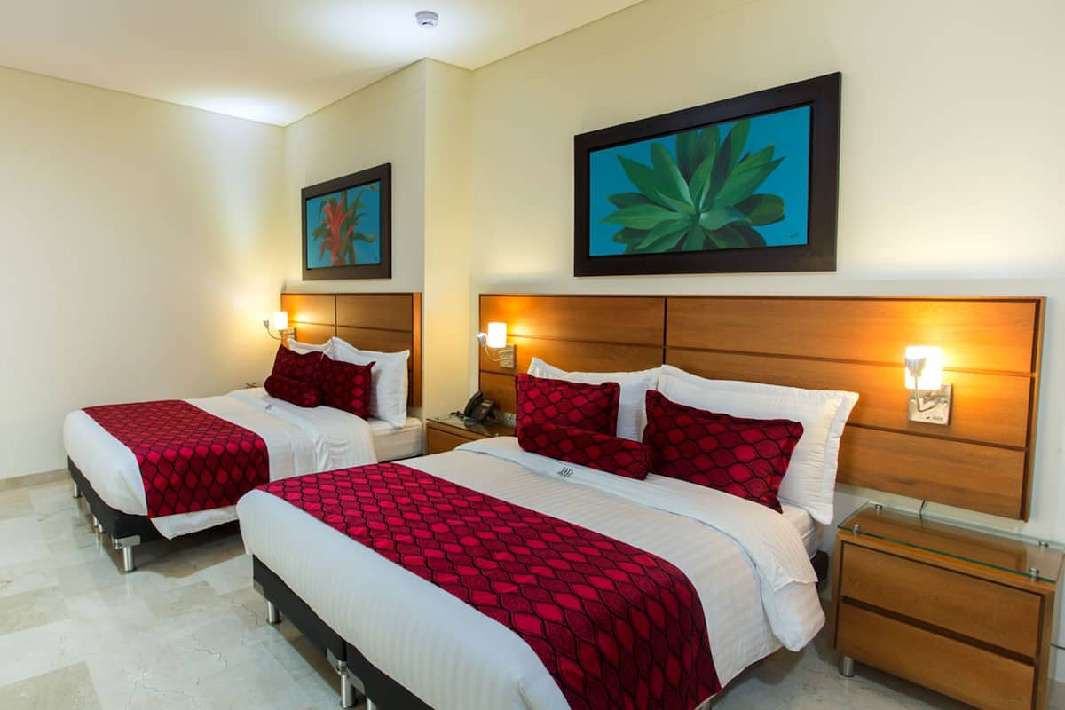 Een hotelkamer met twee bedden, elk met een rood bedovertrek met patroon, witte lakens en passende rode kussens. Er zijn nachtkastjes met lampen, een houten hoofdbord en kunstwerken aan de muur.