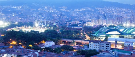 A cityscape with a mix of residential and commercial buildings, a prominent green structure, and a distant mountain range.