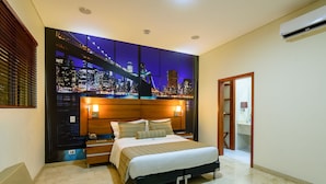 A modern hotel room with a large bed, a cityscape mural on the wall, a wooden headboard, and a walk-in closet.