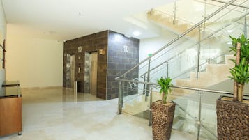 Un hall d’entrée moderne avec un escalier en verre, des ascenseurs et des plantes en pot.