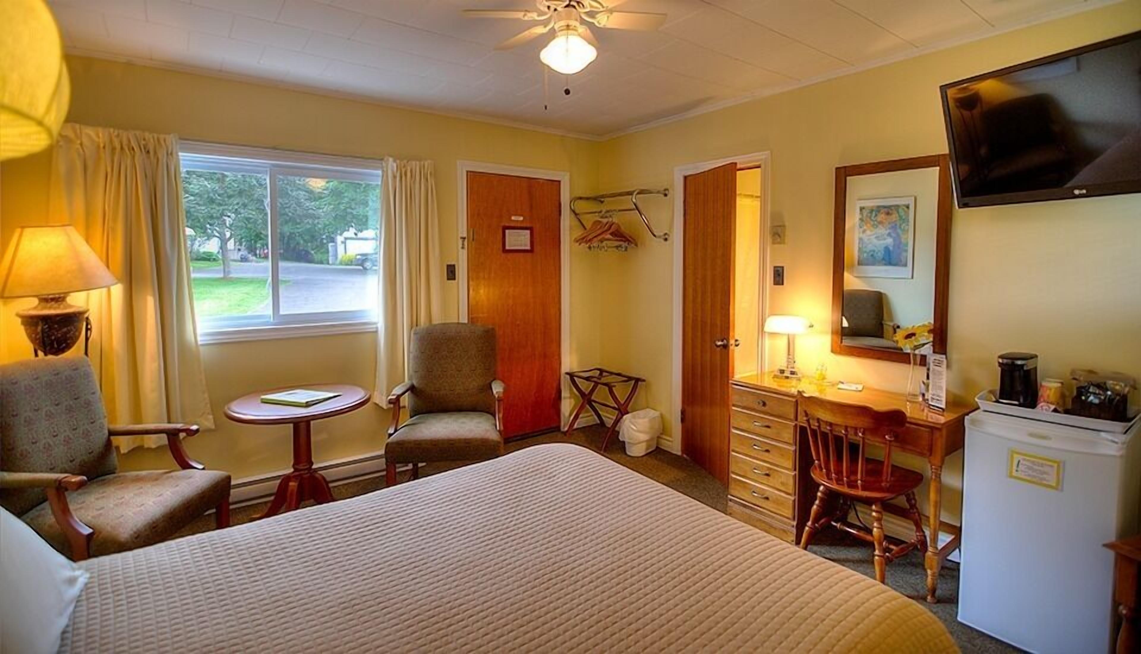 A hotel room with a bed, two chairs, a desk with a chair, a television, and a window with curtains.