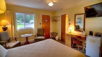 A hotel room with a bed, two chairs, a desk with a chair, a television, and a window with curtains.