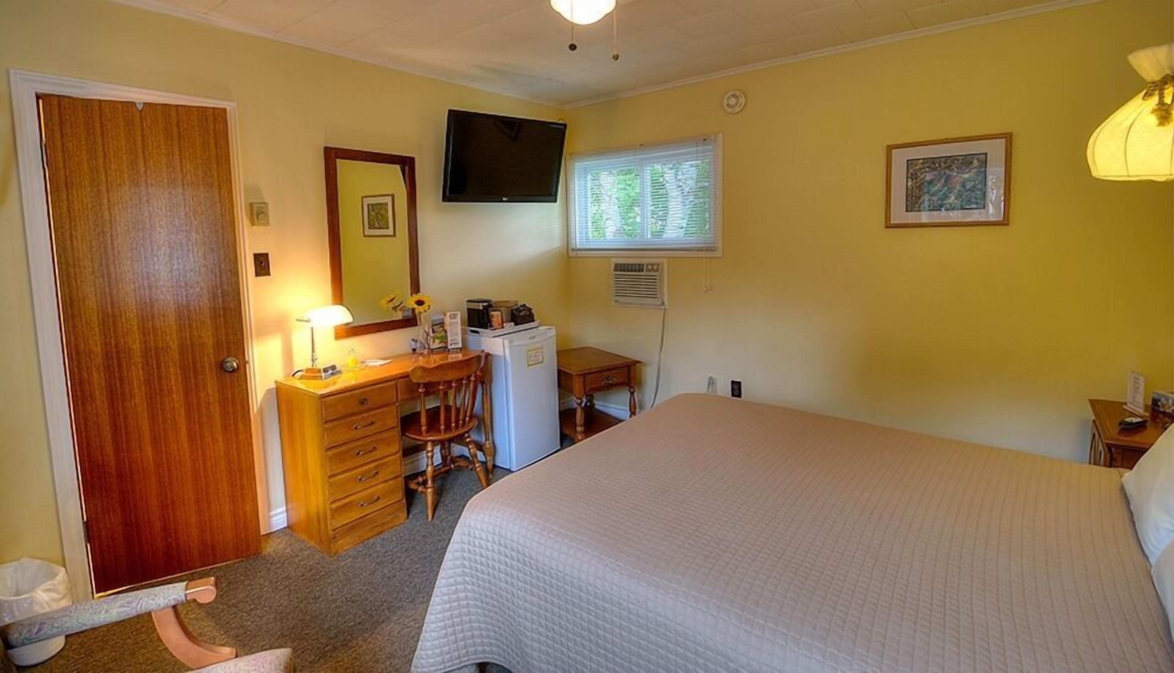 A bedroom with a bed, a dresser, a desk, a television, and a window with blinds.