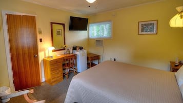 A bedroom with a bed, a dresser, a desk, a television, and a window with blinds.