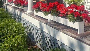 Un porche con columnas blancas, flores rojas y techo de madera.