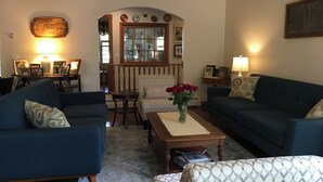 Una sala de estar acogedora con dos sofás, una mesa de centro y un reposapiés estampado. Un jarrón con flores rojas añade un toque de color.