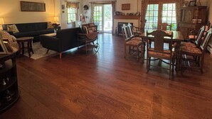 Un salón espacioso con un sofá verde oscuro, una mesa de comedor de madera con sillas y una araña.