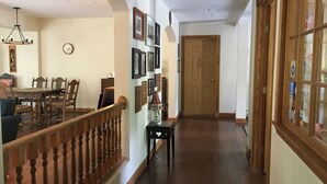 Un pasillo con baranda de madera, un comedor con mesa y sillas, y una puerta al final.