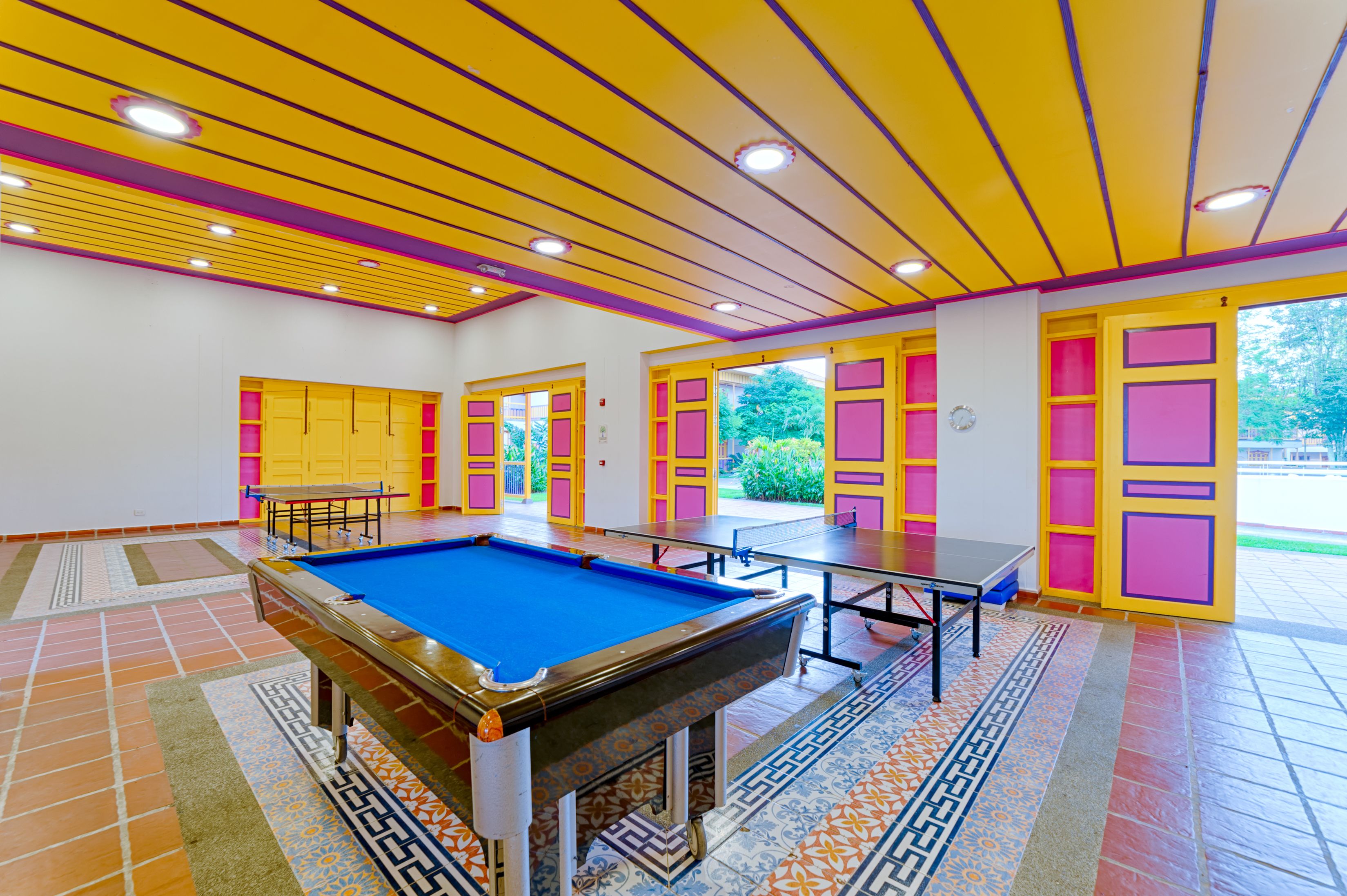 Een pooltafel in een vrolijk gekleurde kamer met een betegelde vloer en een plafond met gele en paarse strepen.