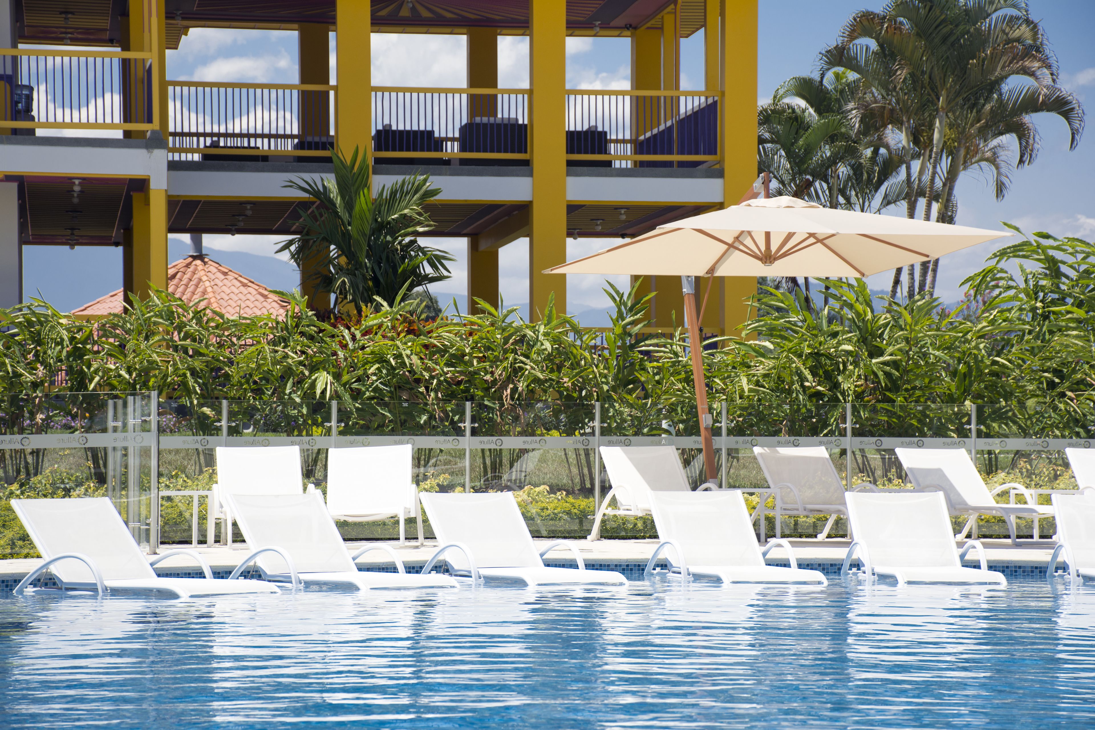 A swimming pool with white lounge chairs and a beach umbrella.