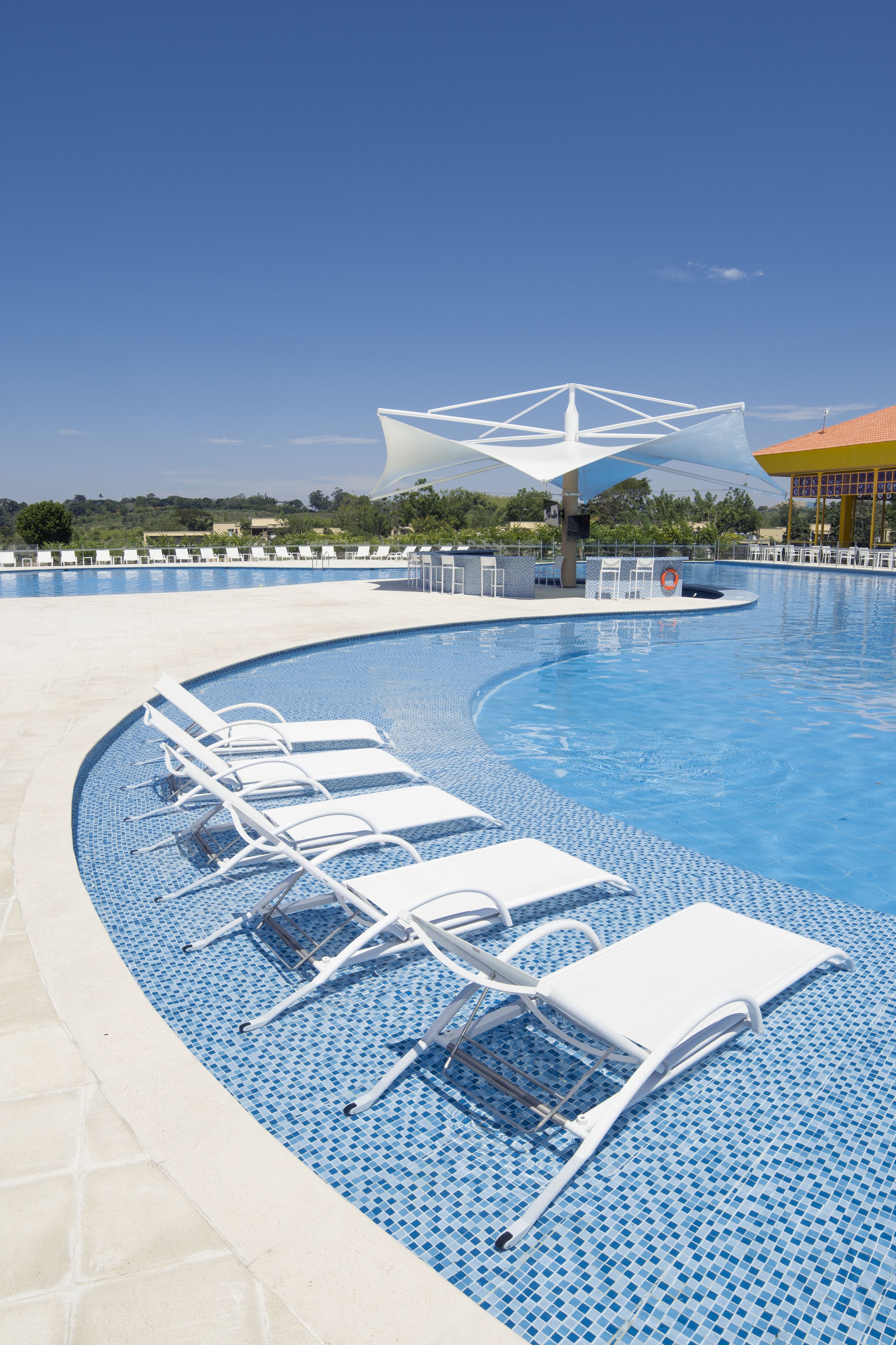 A swimming pool with white lounge chairs and a sun umbrella.