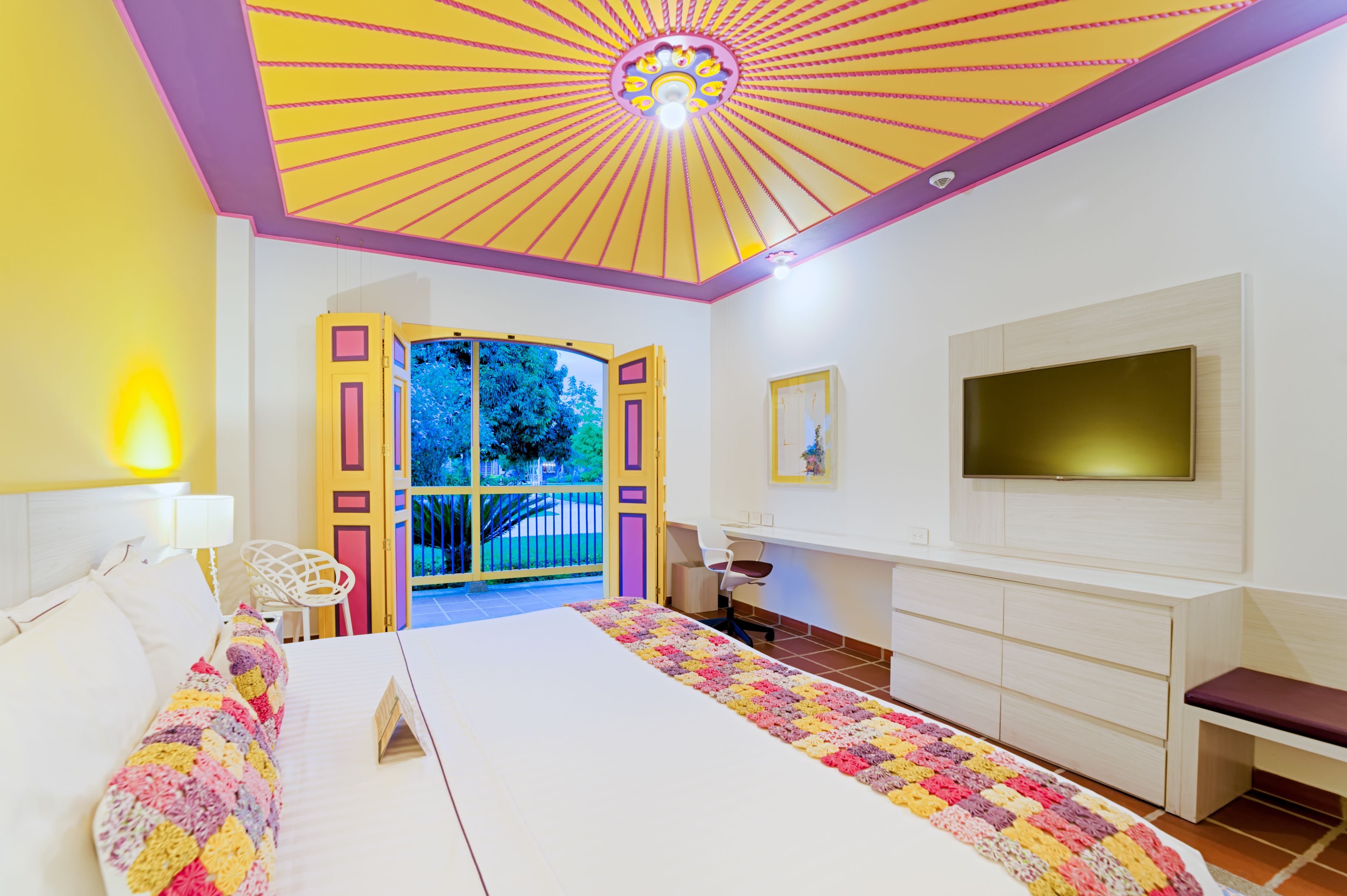 Un dormitorio con una cama grande, un escritorio, un televisor y vistas al exterior.