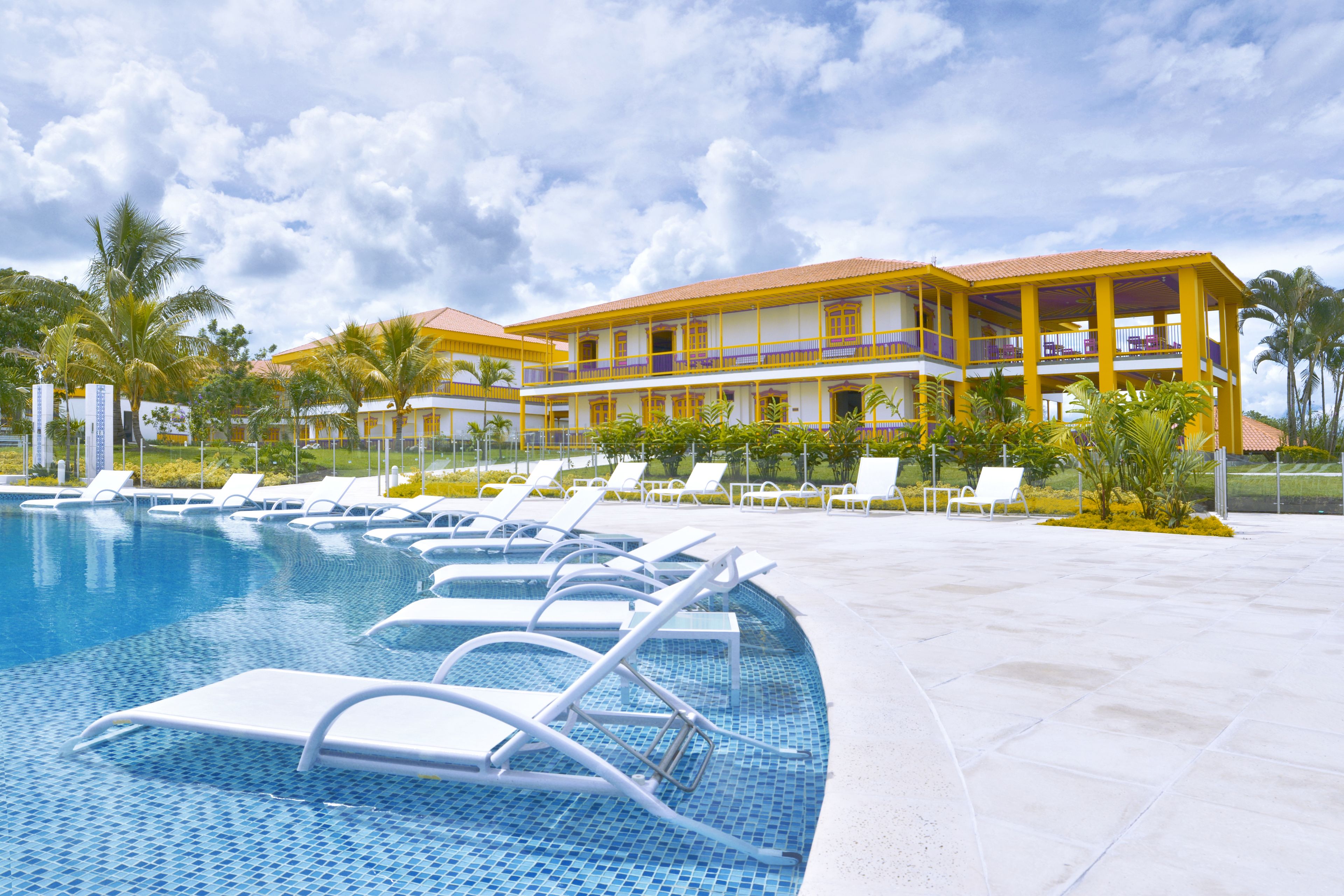 Un hotel con piscina, varias sillas de descanso y un edificio de dos pisos con balcones.