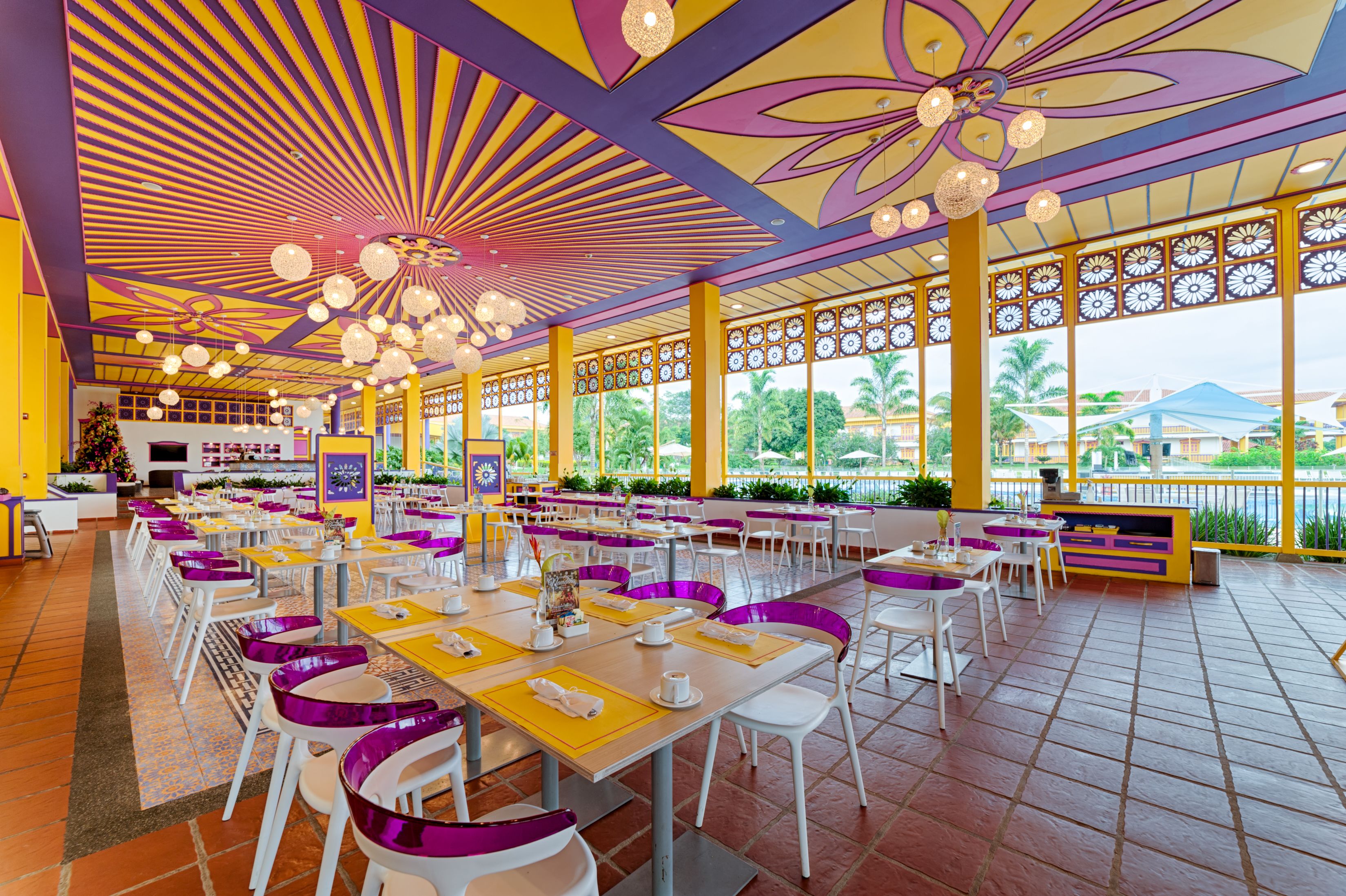 A spacious dining area with yellow and purple decor, large windows, and a view of palm trees.