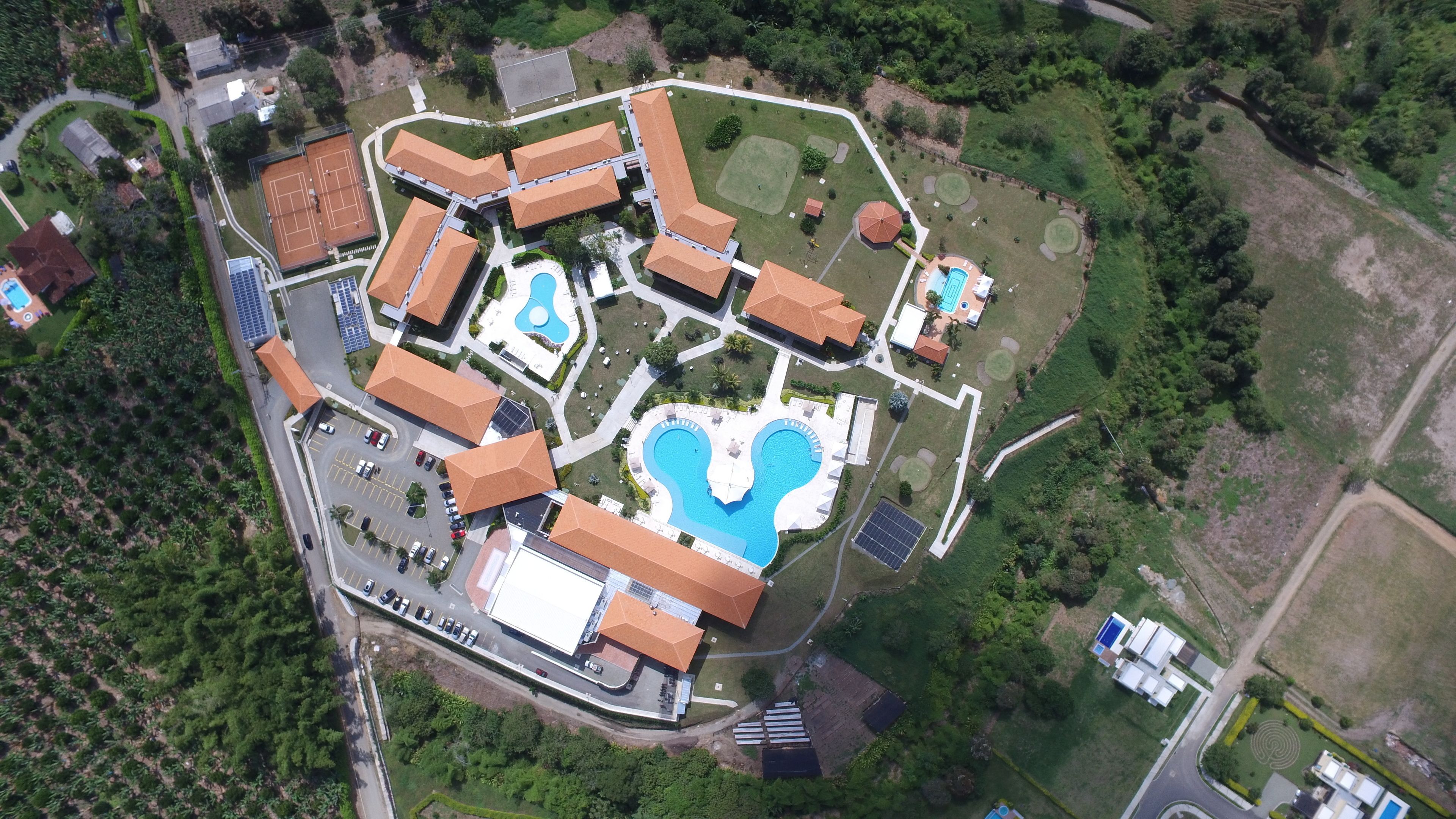 Vista aérea de un complejo turístico con varias construcciones, piscina y follaje circundante.