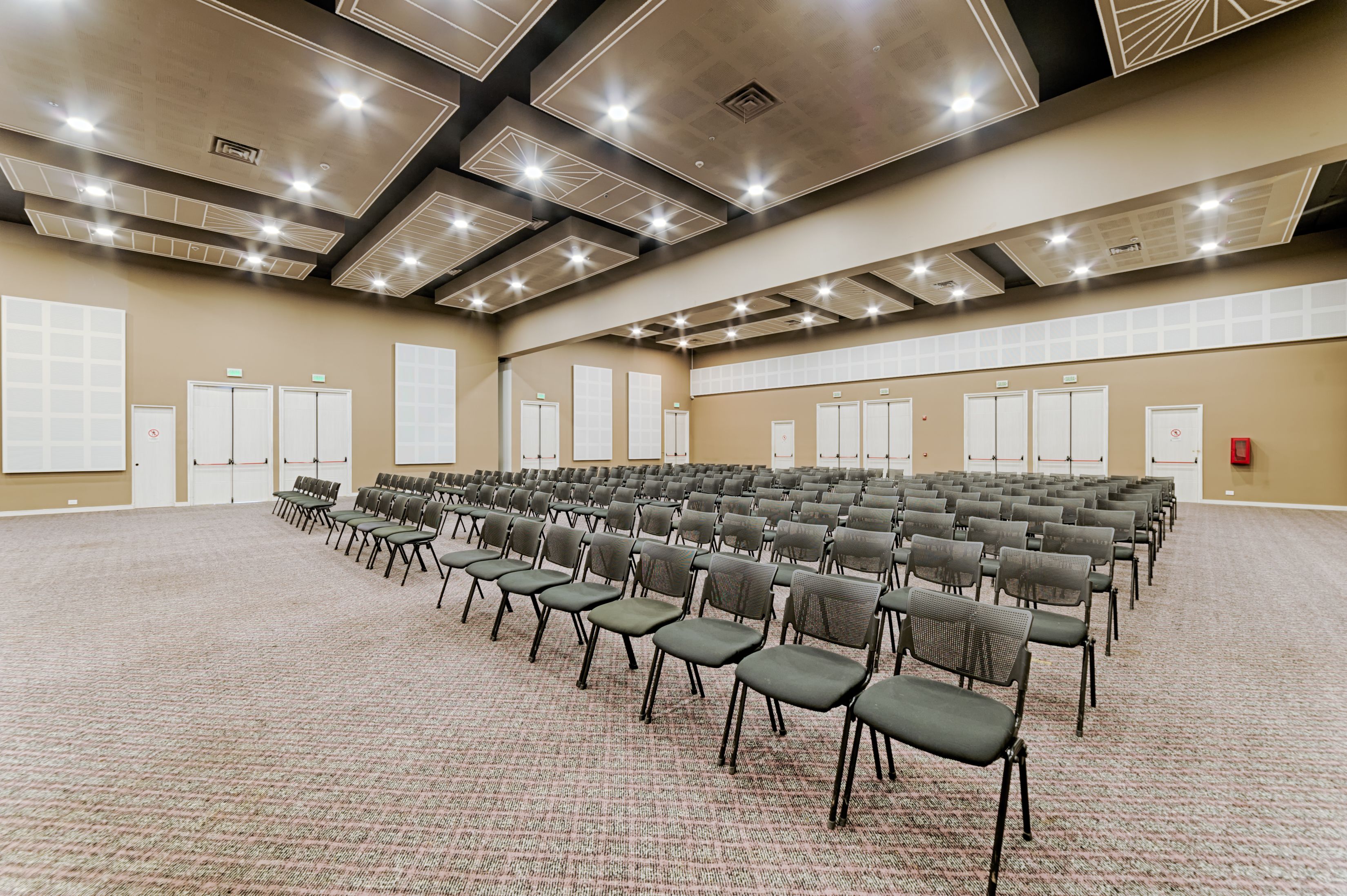 A large conference room with rows of chairs, carpeted floor, and a high ceiling with recessed lighting.