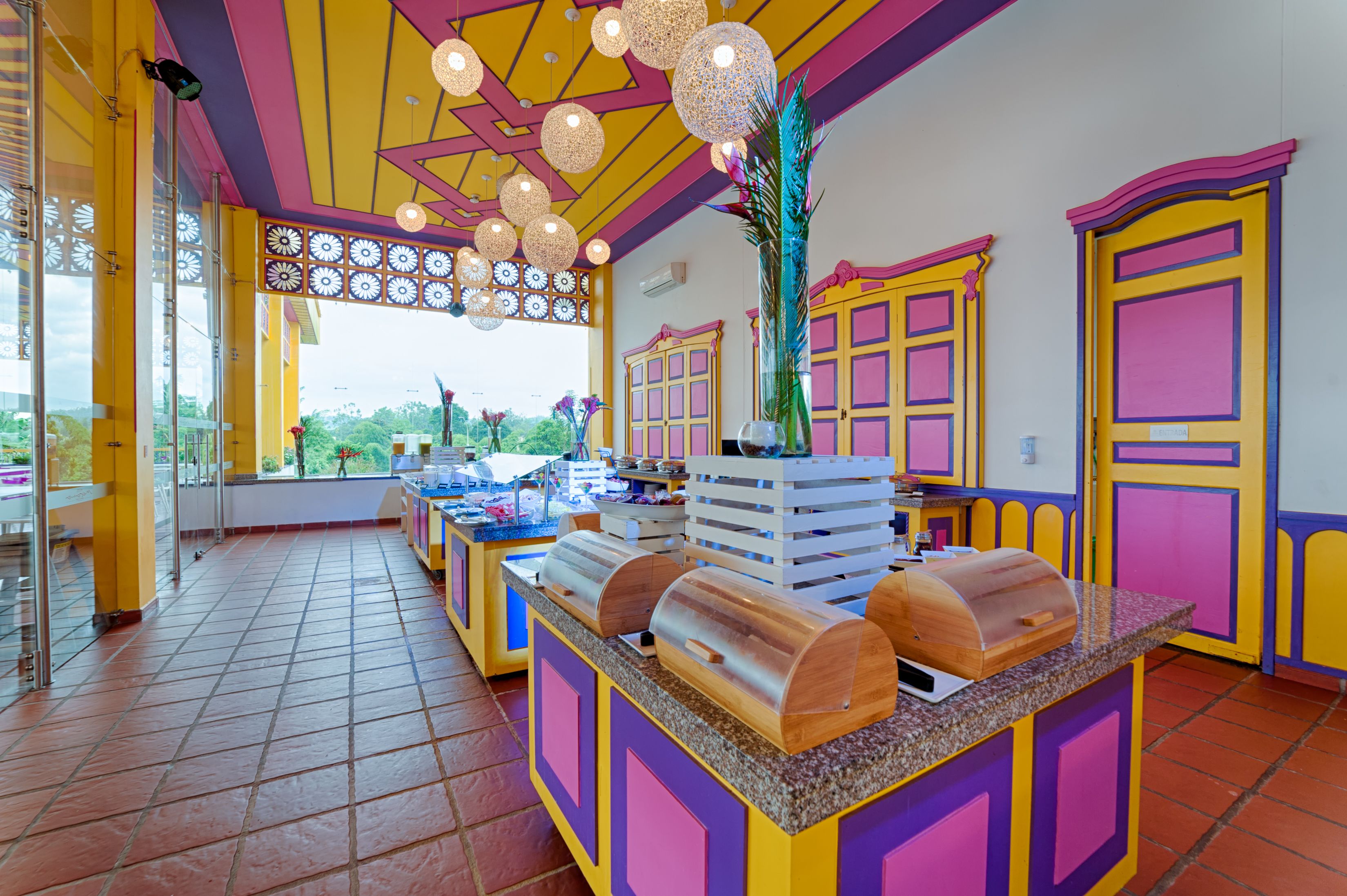 Uma área de buffet colorida com diversas estações de comida e uma grande janela com vista para o exterior.