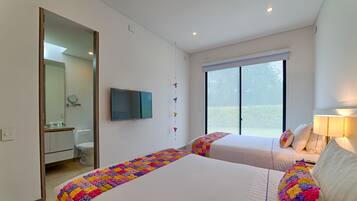 Quarto de hotel com duas camas, televisão, janela com persianas e banheiro visível através de uma porta aberta.