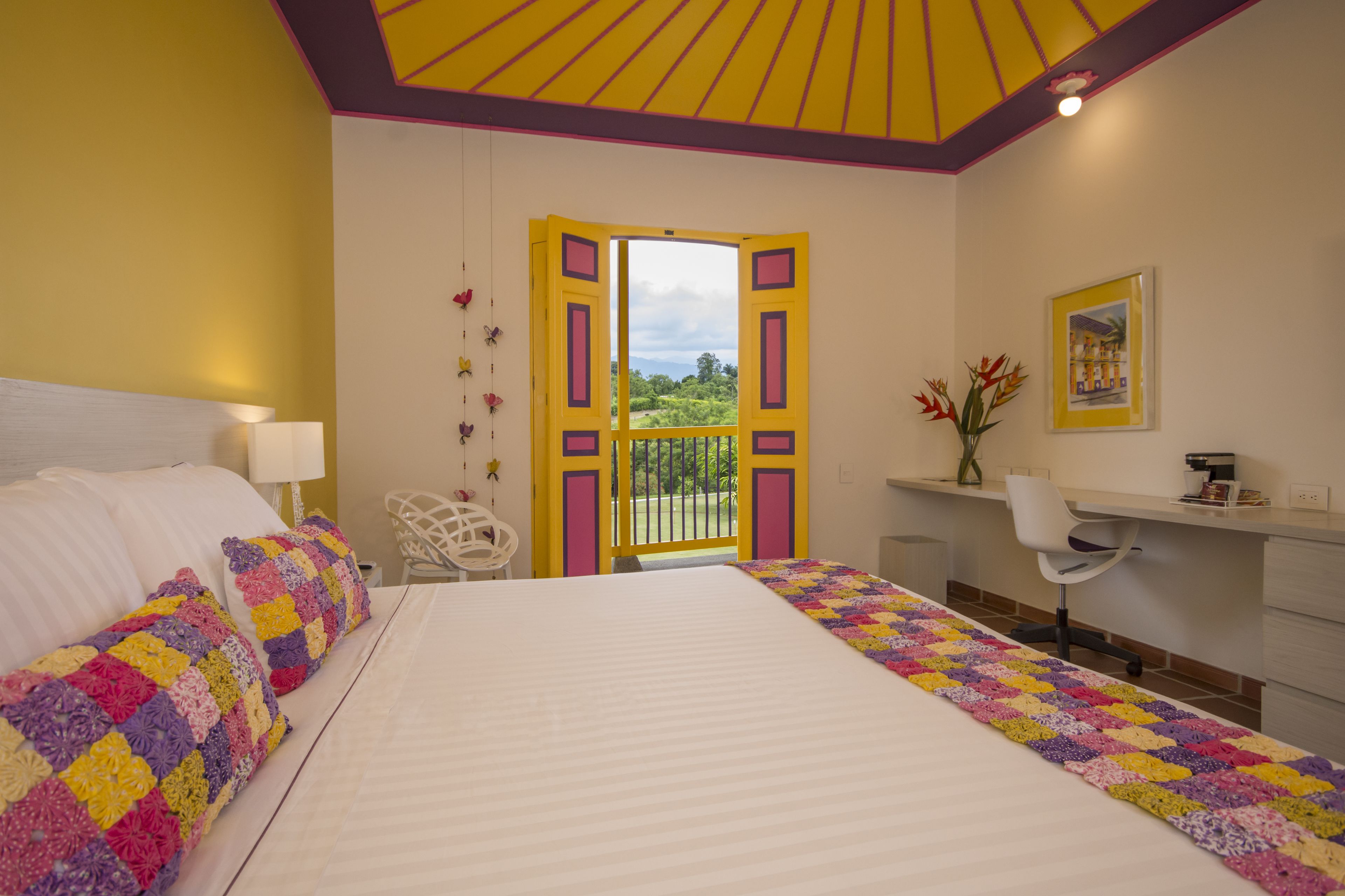 A bedroom with a bed, a desk, and a view of the outdoors.